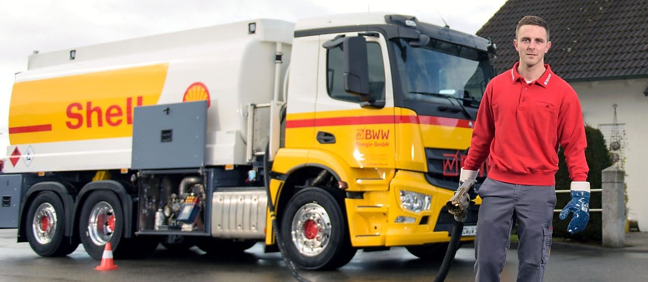 Junger Tankwagenfahrer steht vor Tankwagen und traegt Schlauch