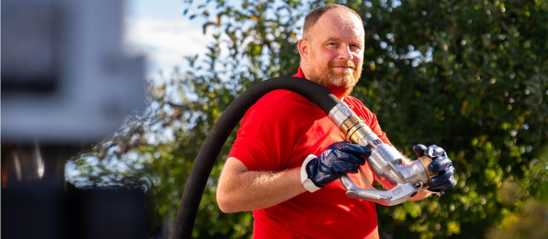 Junger Tankwagenfahrer steht vor Tankwagen und traegt Schlauch