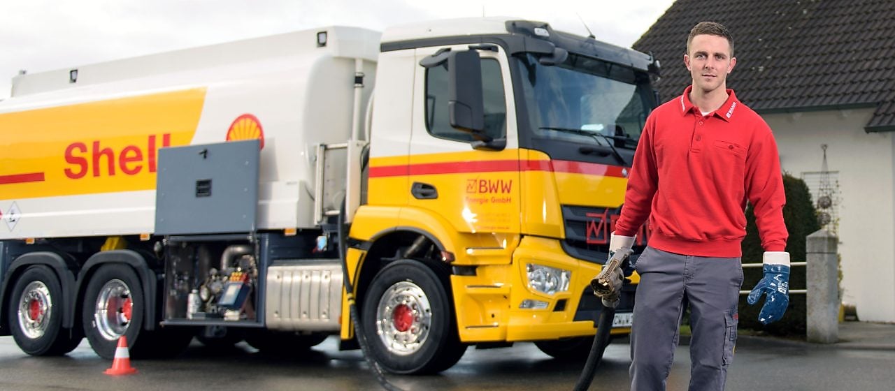 Junger Tankwagenfahrer steht vor Tankwagen und traegt Schlauch