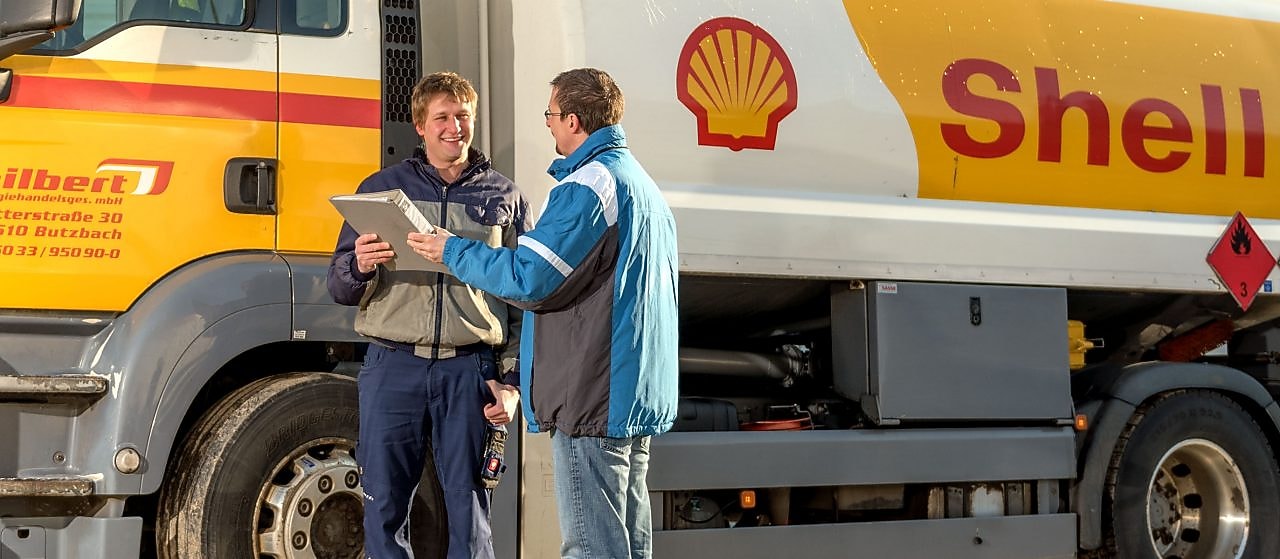 Zwei Mitarbeiter überprüfen Papiere neben Shell Tankwagen