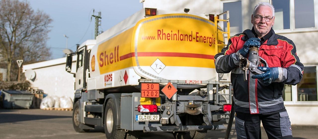 Tankwagenfahrer steht vor Shell Tankwagen und traegt Schlauch